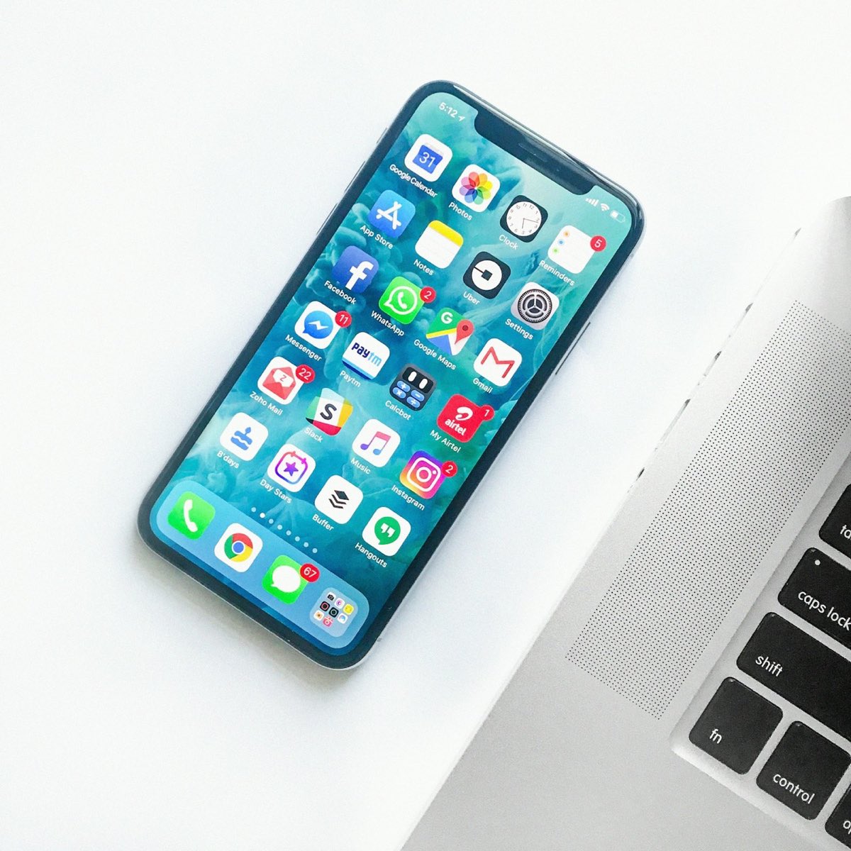 An iPhone beside a laptop on a clean white desk — mobile and desktop development side by side